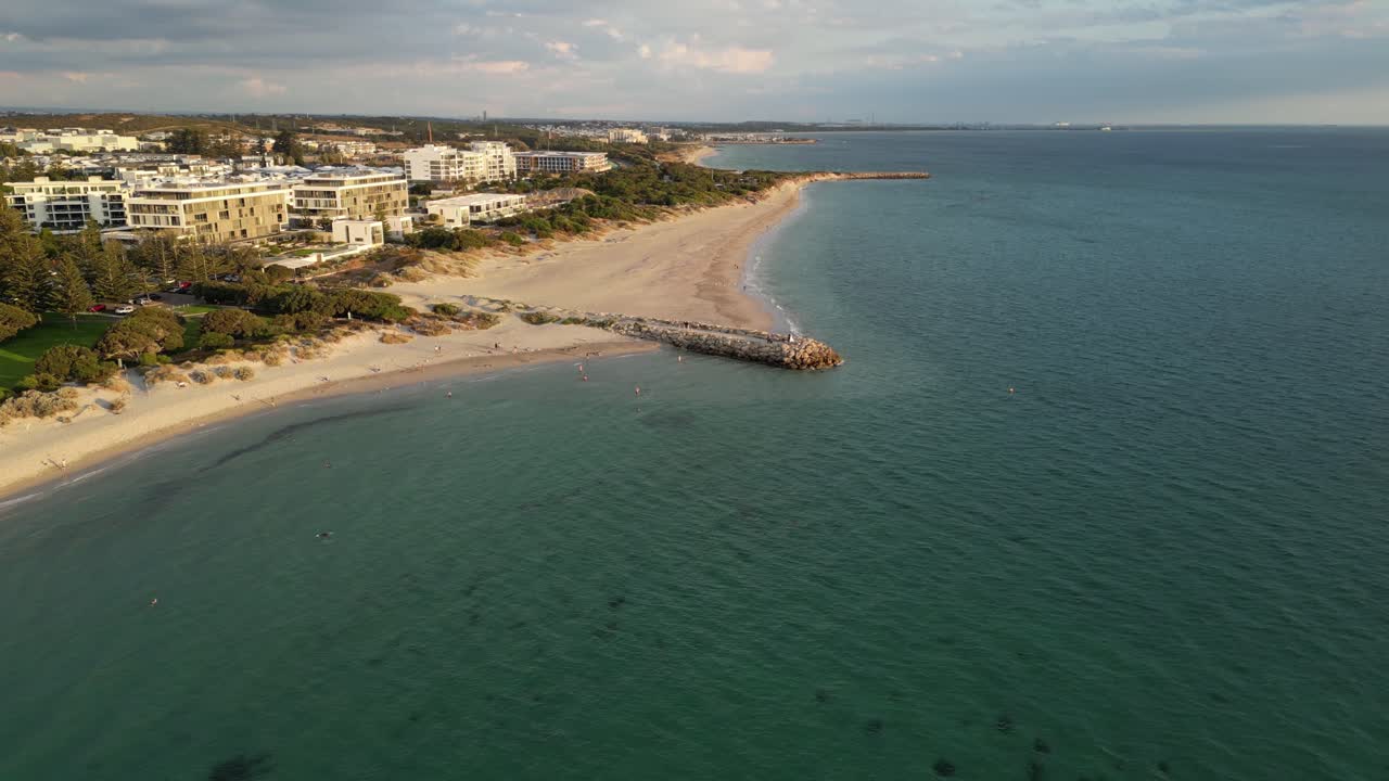 tomada aérea del hermoso océano, la playa de arena y la ciudad de fermantle con edificios de lujo por la puesta de sol dorada en australia occidental