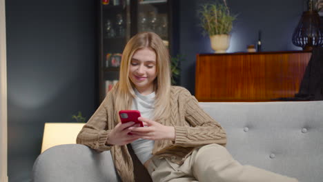 happy young woman chatting on smartphone and laughing while sitting on a couch at home 1