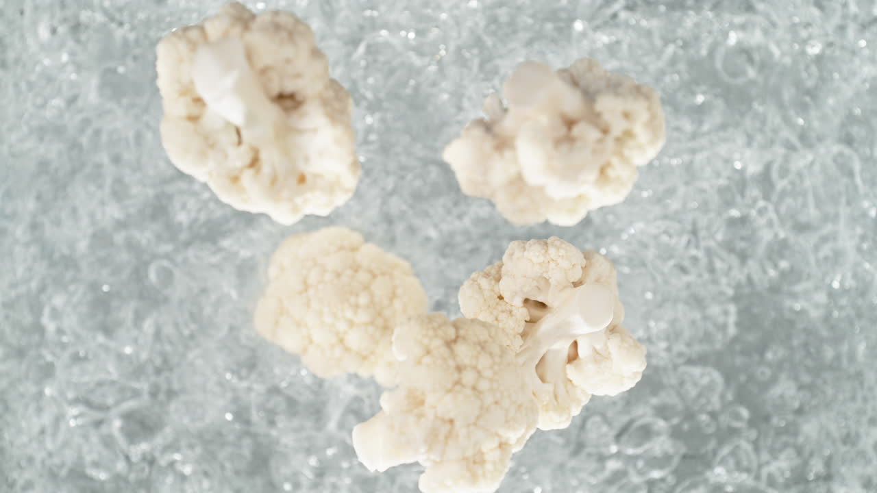 Cauliflower Florets Falling Into Pot Of Boiling Water Making A Splash in Slow Motion, Table Top View