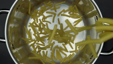 macaroni bag being poured in slow motion into an empty metal pot, seen from the top