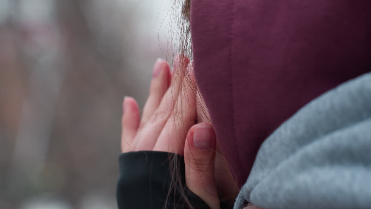 차가운 날씨에 검은 긴 팔로 코를 는 젊은 여성의 근접 측면 얼굴 뷰, 그녀의 은 피부는 겨울 추위를 강조합니다, 나무의 흐릿한 배경