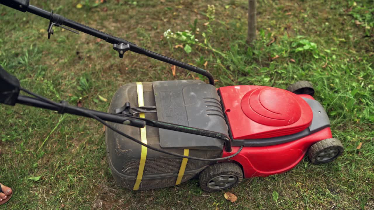Woman is cutting lawn with grass mower. Gardener with electric lawn mower trimming grass in the yard in summer.