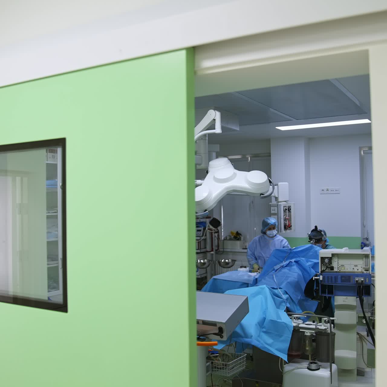 Cirujano trabajando solo con la ayuda de una enfermera en una moderna sala de operaciones bien equipada. Mirando hacia las puertas del quirófano contemporáneo.