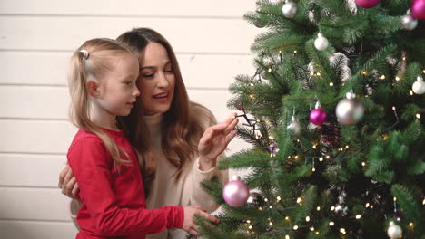 madre con su hija colgando adornos navideños en el árbol de navidad 1