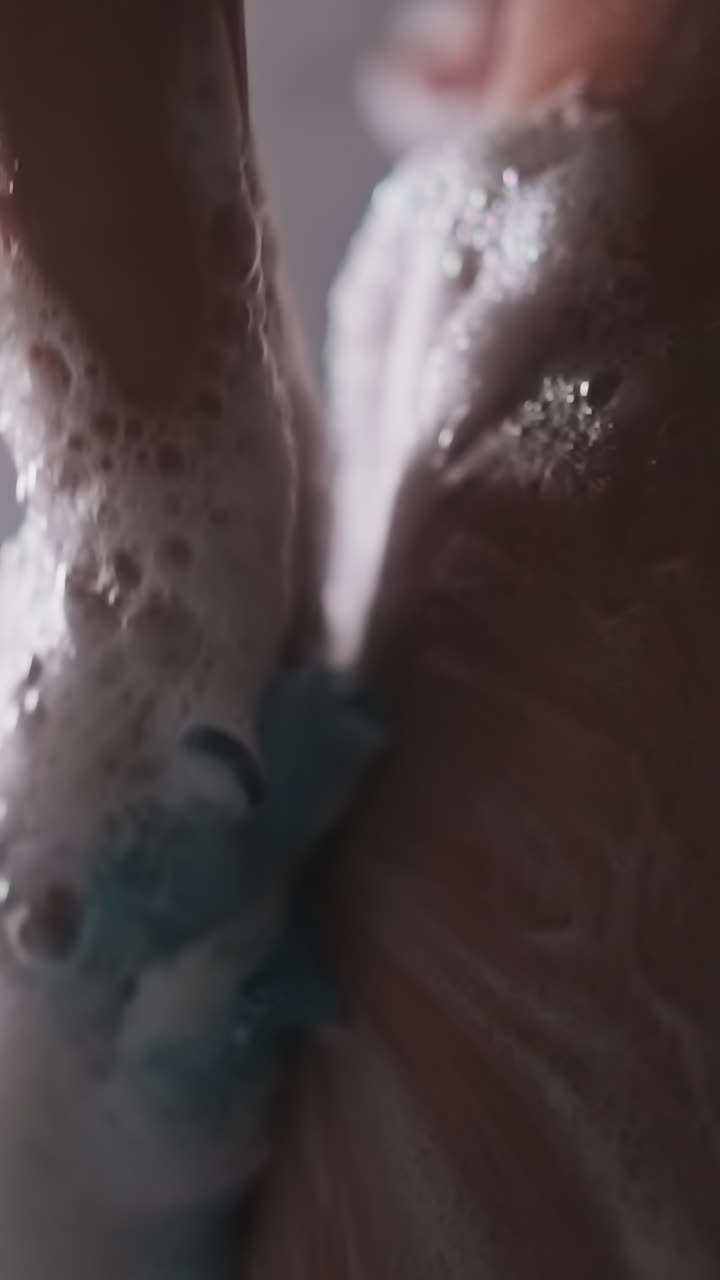 la mujer se lava con la lúpula en el cubículo de la ducha en primer plano. la dama frota la piel del cuerpo con una esponja espumosa suave cerca de los pulverizadores de agua. rituales higiénicos en el hogar