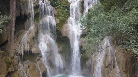 rising jungle aerial reveals man on tier of kuang si waterfall, laos