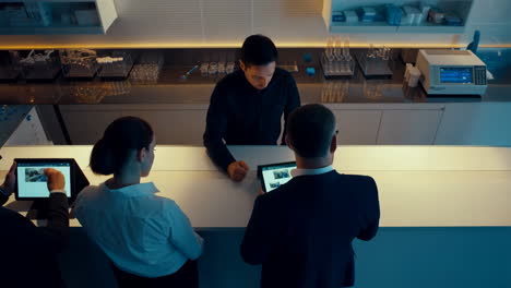 four individuals engaged with tablets at a sleek, modern bar or lab lounge setting
