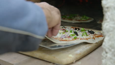 Hand-carefully-scoops-pizza-onto-paddle-and-places-in-brick-oven,-close-up