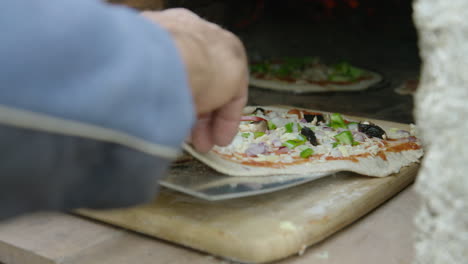 hand carefully scoops pizza onto paddle and places in brick oven, close-up