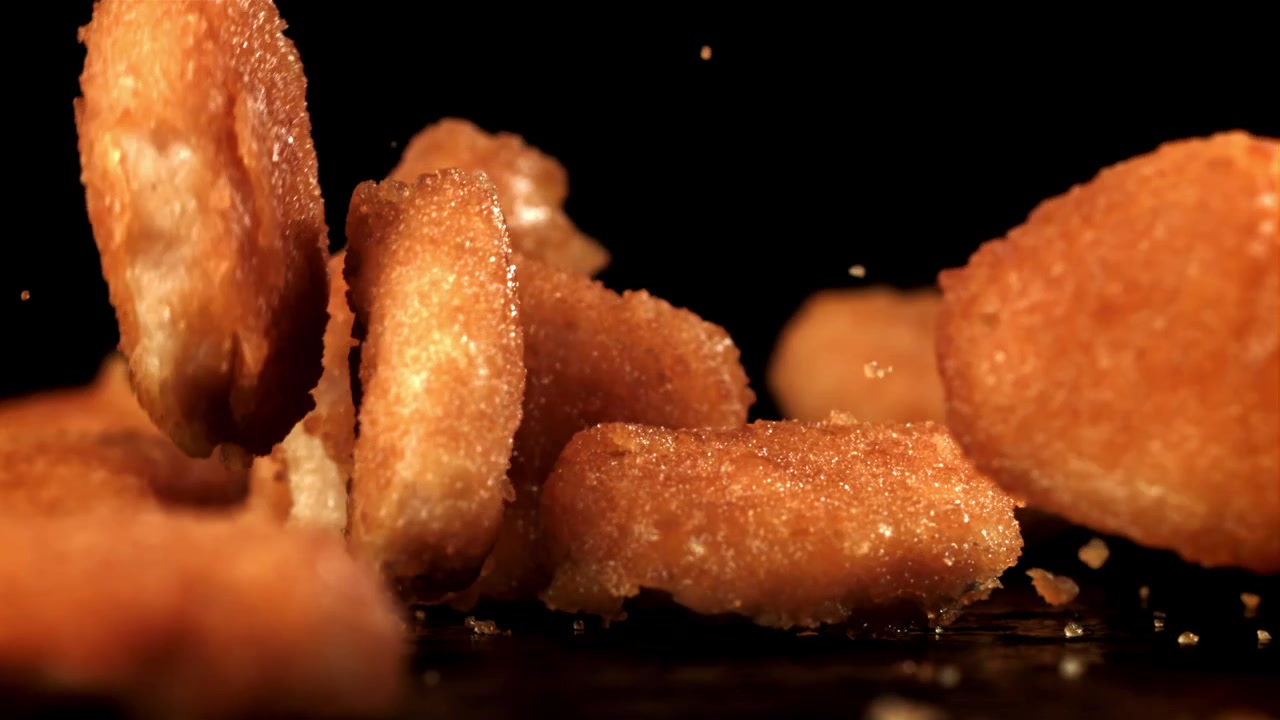 Nuggets de pollo dorados cayendo en cámara lenta.