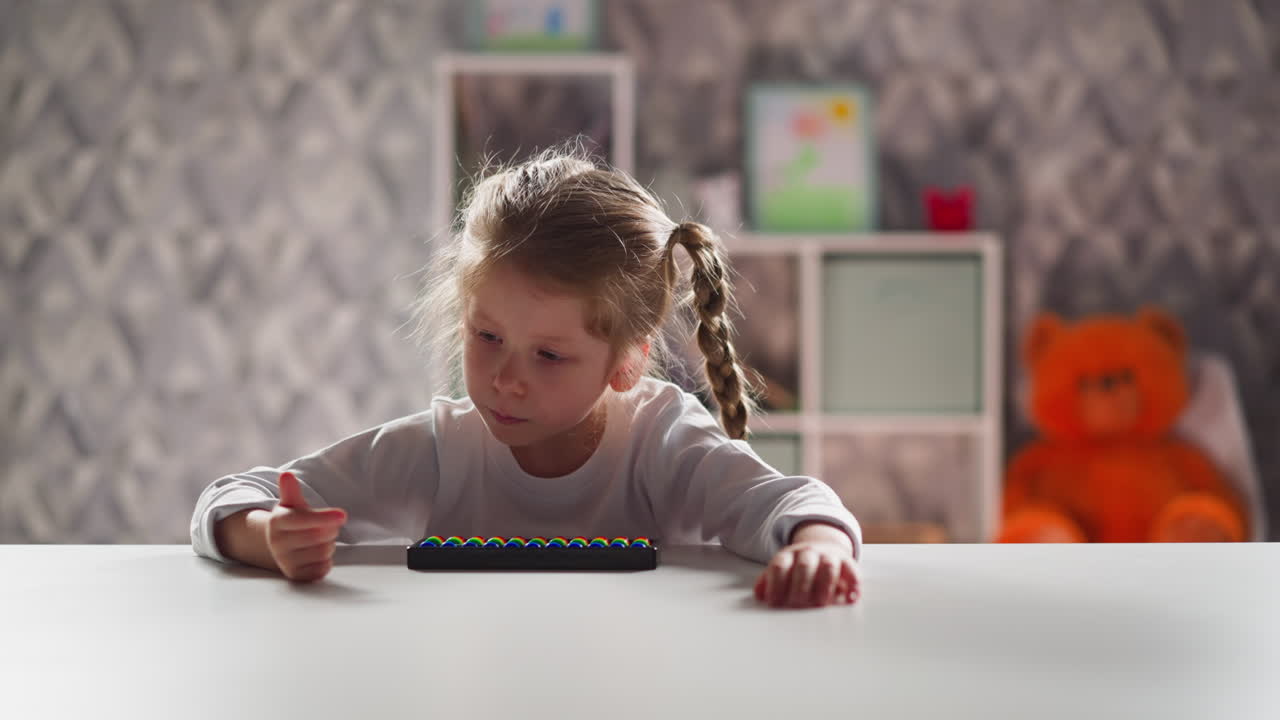 Una bambina attiva con un abaco conta con il dito e parla alla scrivania.