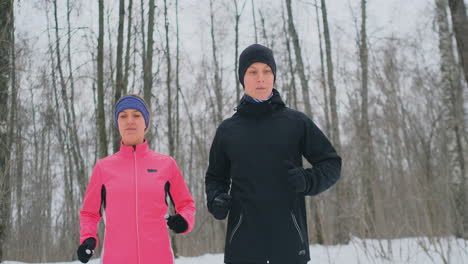 positive beautiful young healthy couple running with sportswear through the forest in the sunny winter morning.