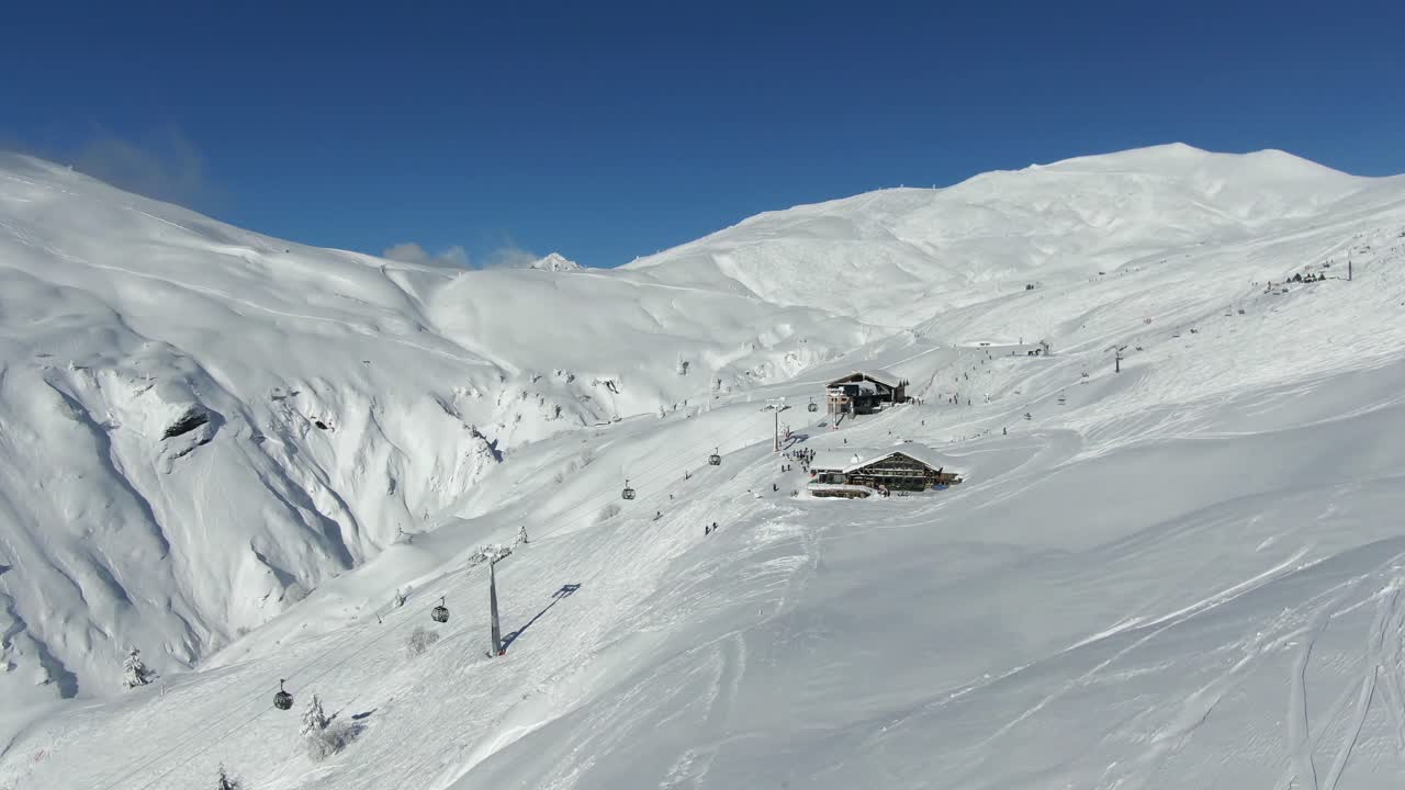 vuelo de avión no tripulado sobre chalet y silla de elevación con esquiadores en la ladera soleada de la montaña bajo un cielo azul
