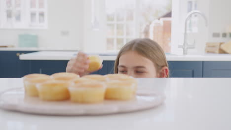 Nahaufnahme-Eines-Teenager-Mädchens,-Das-Zu-Hause-In-Der-Küche-Nach-Frisch-Gebackenen,-Hausgemachten-Cupcakes-Vom-Teller-Greift