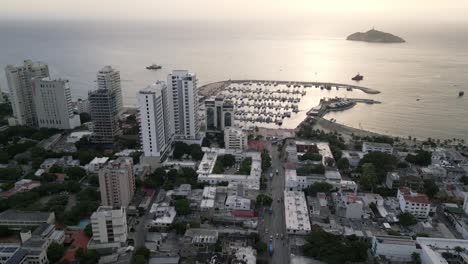 toma de drones de santa marta, colombia, tráfico de la ciudad, edificios frente al mar y puerto deportivo a la luz del sol de la hora dorada.