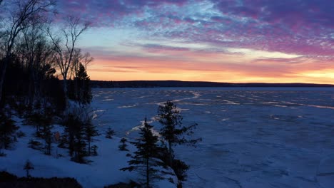 aerial, dramatic orange and pink clouds at dawn at a frozen lake during winter