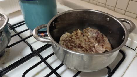 succulent beef steaks seared in steel pan over gas flame