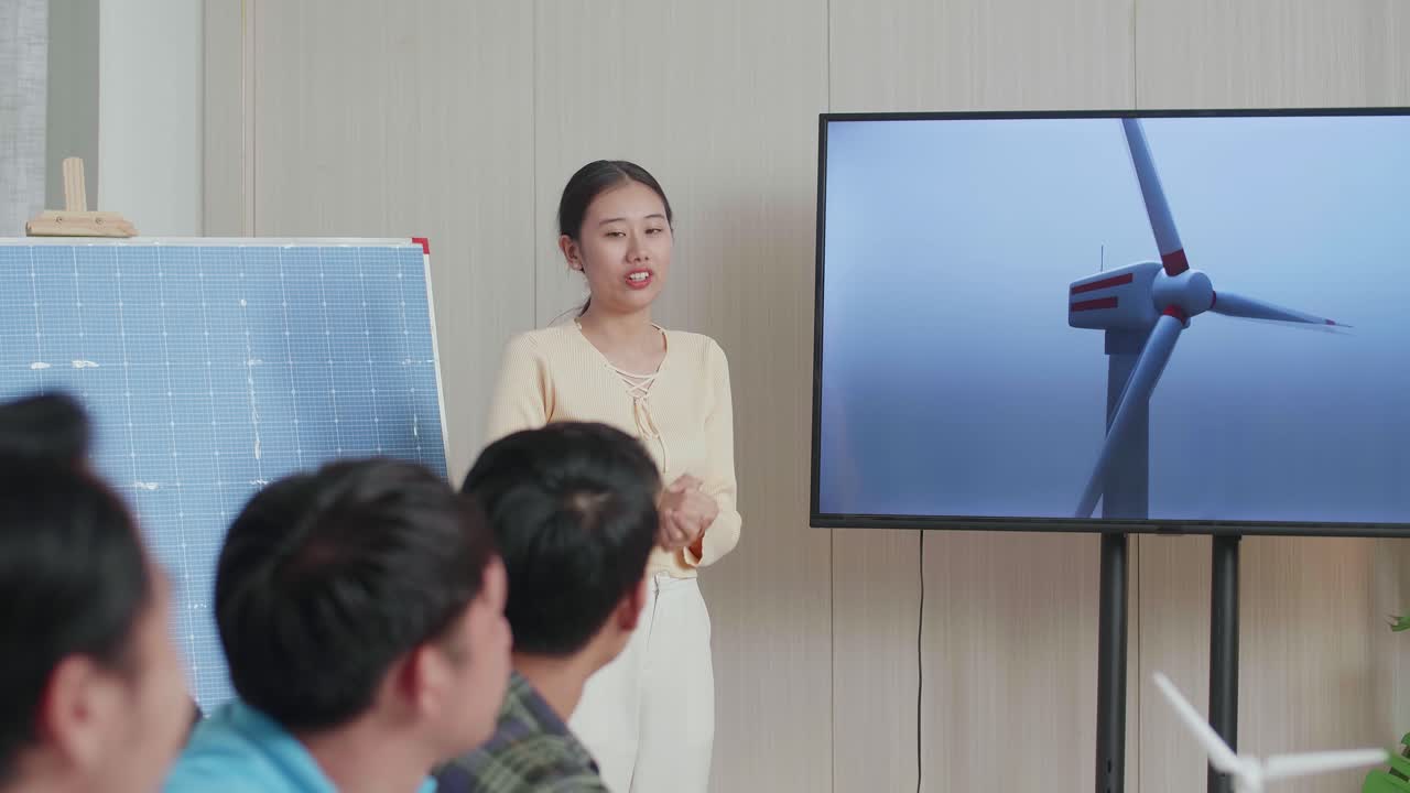 태양전지를 가진 아시아 여성 엔지니어가 사무실에서 풍력 터빈에 대한 프레젠테이션을 성공시켰고, 관객들은 박수를 치며 인상적이라고 느습니다.