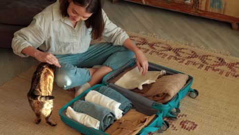 young travel woman and cat packing clothes into suitcase