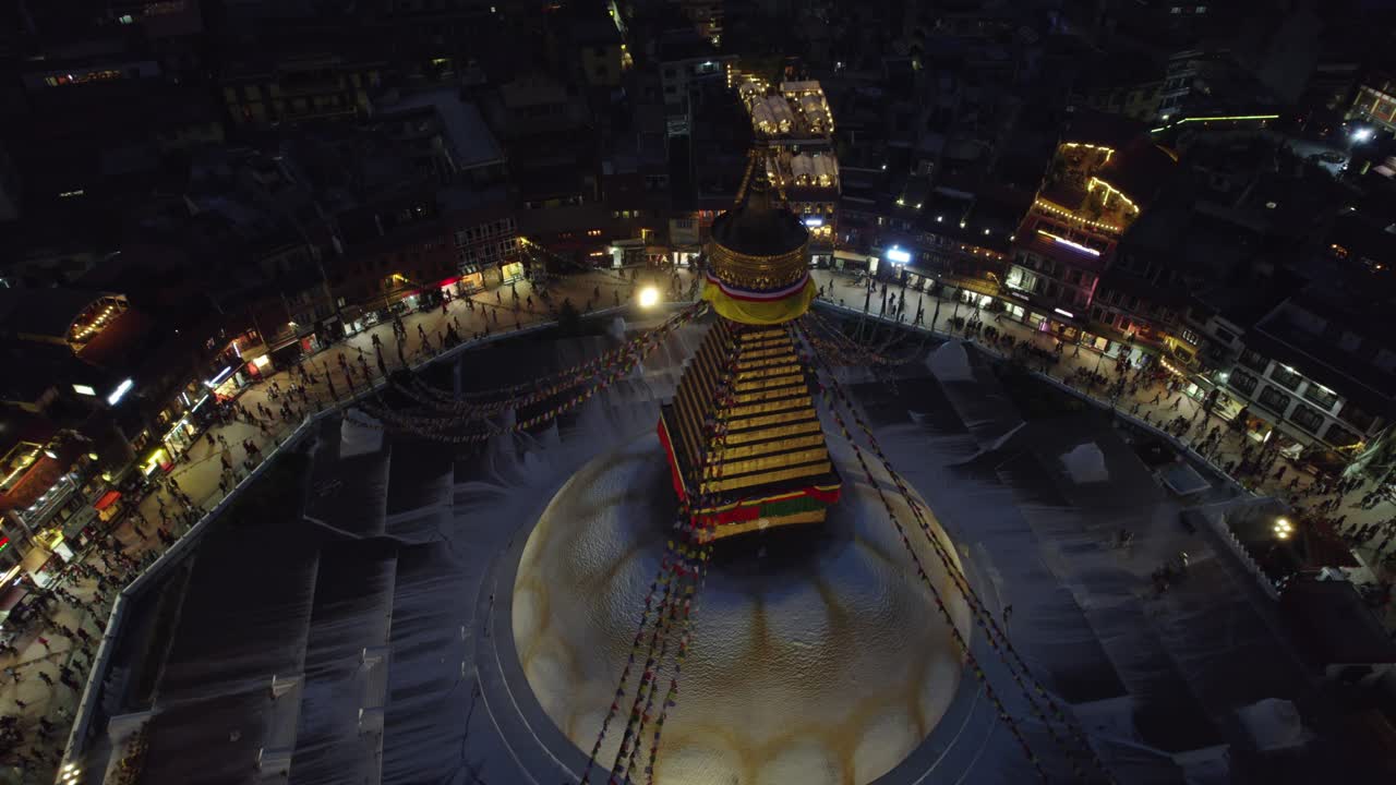 A serene night drone view of Boudhanath Stupa, also known as boudha nath, glowing above Kathmandu. The sacred Buddhist landmark stands radiant against the quiet urban nightscape