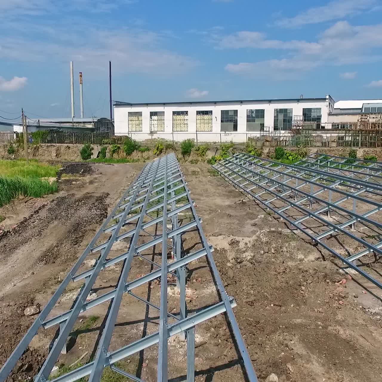 Installed metal supports on the field prepared for solar panels. Footage along the construction site with industrial zone at backdrop