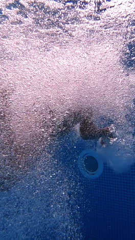 Young boy jumps underwater into a pool. Underwater shot with amazing bubbles inside the swimming pool. Boy in blue water with beautiful bubbles splash. Vertical video