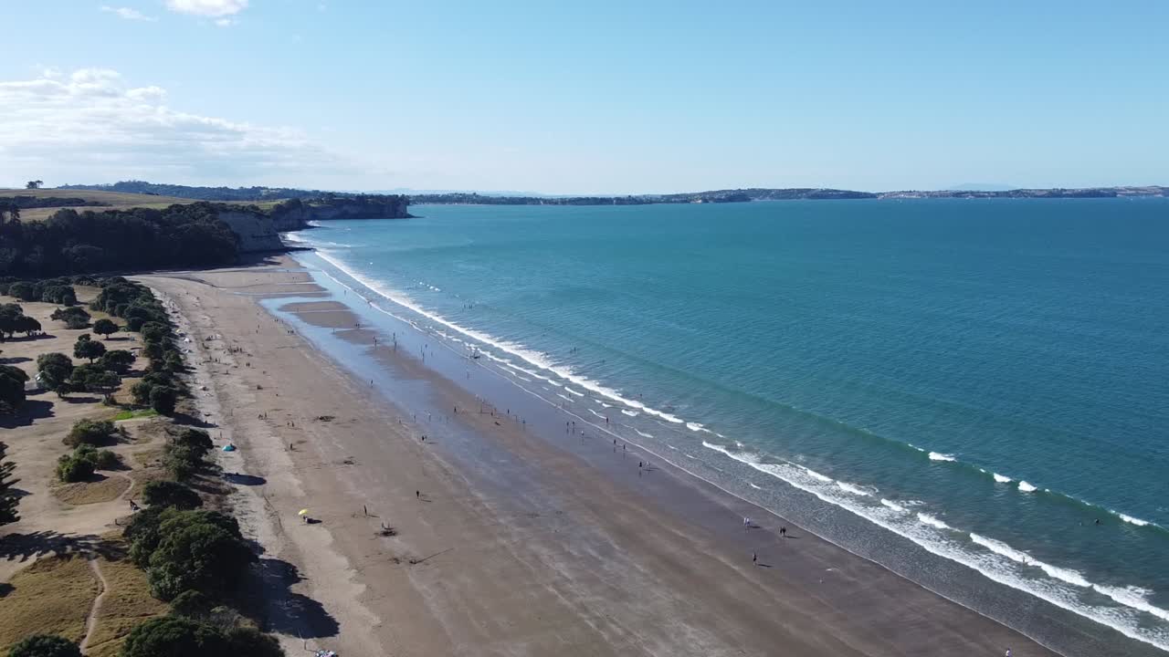 toma aérea, volando sobre una hermosa playa con gente en un día soleado en long bay, nueva zelanda