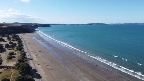 Toma-Aérea,-Volando-Sobre-Una-Hermosa-Playa-Con-Gente-En-Un-Día-Soleado-En-Long-Bay,-Nueva-Zelanda