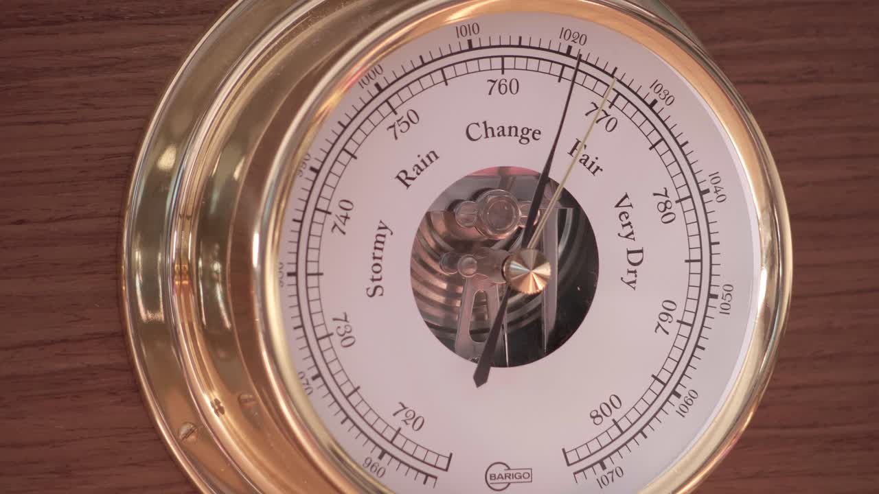 Circular brass barometer showing weather conditions from stormy to fair with scientific markings and metallic needle. Macro detail shot