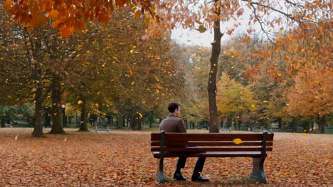 man sitting alone on park bench in autumn