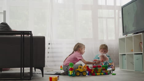 little boy watches sister shaking baby doll sitting on floor