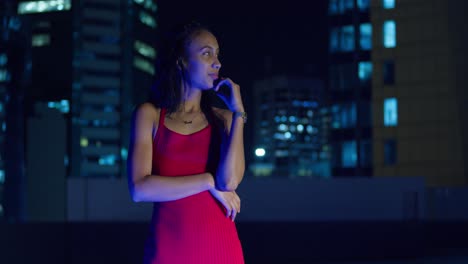 El-Cielo-Nocturno-Enmarca-A-Una-Joven-Con-Un-Vestido-Rojo-En-Una-Azotea,-Con-Edificios-De-La-Ciudad-A-Lo-Lejos