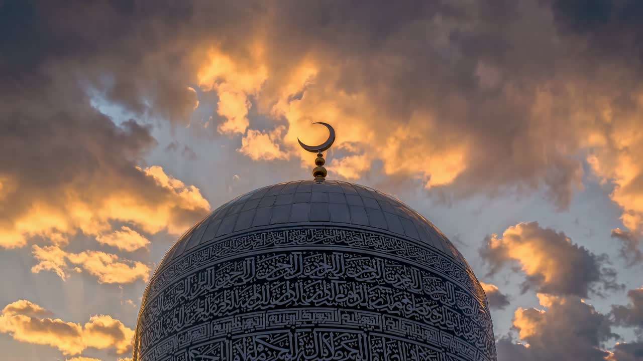 Uma filmagem em vídeo em ângulo baixo da cúpula de uma mesquita com caligrafia complexa, tendo um pôr do sol dramático como plano de fundo