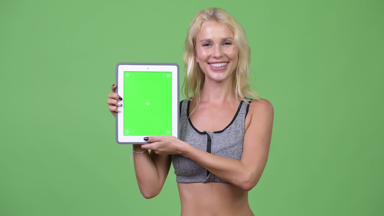 Giovane donna felice e bella che mostra un tablet digitale, pronta per la palestra