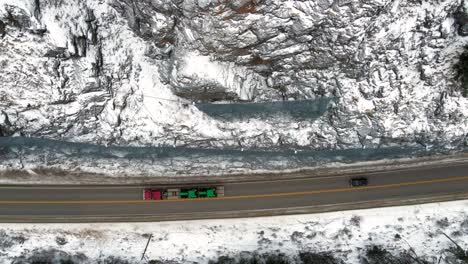 overhead shot of an red semi truck hauling green tractors on highway 5 in the north thompson river valley near kamloops along a tight road and protected rockfaceside