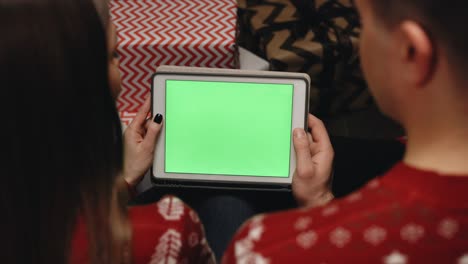 manos sosteniendo una tableta con pantalla de maquillaje verde. pareja caucásica usando tableta para video llamada de navidad con pareja feliz en la pantalla. navidad, festividad y tecnología de comunicación
