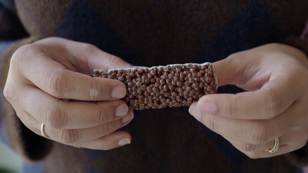 Hands Holding a Chocolate Puffed Rice Snack Bar with White Topping
