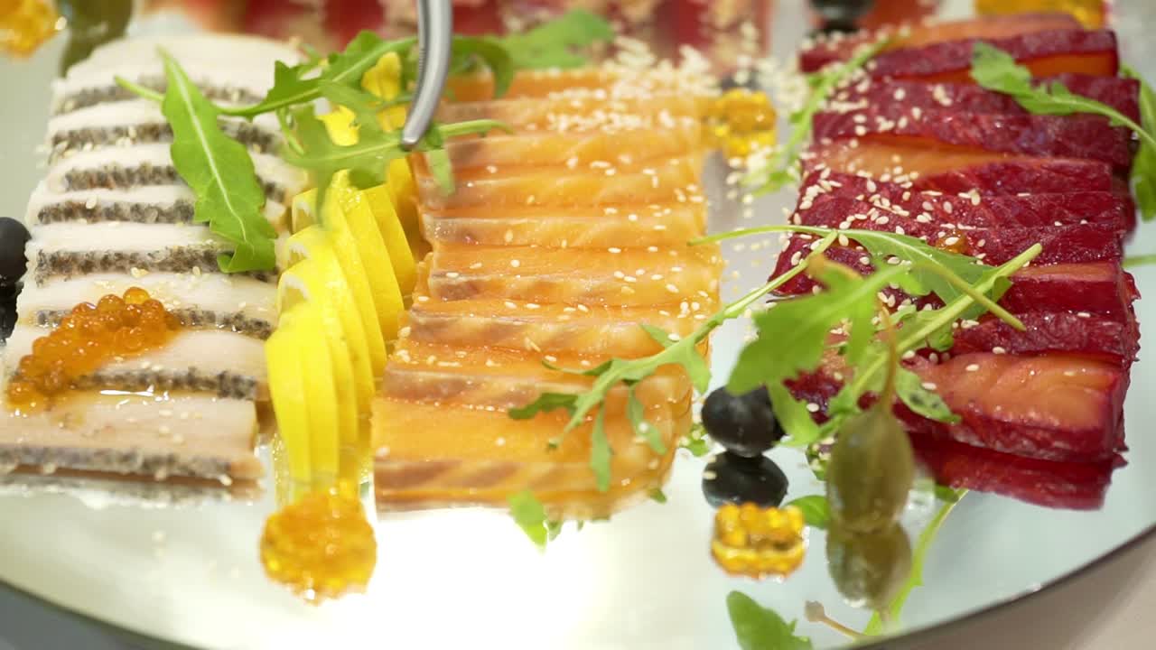 Serving sliced with dried and smoked meat, red fish fillet, hard cheese decorated with olives, red caviar, cherry tomatoes, lemon slices and cilantro leaves nearby. Close-up.