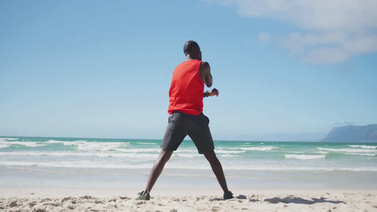 African american man stretching on the beach, exercising outdoors by the sea