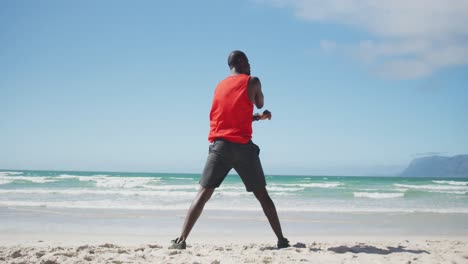 Hombre-Afroamericano-Estirándose-En-La-Playa,-Haciendo-Ejercicio-Al-Aire-Libre-Junto-Al-Mar