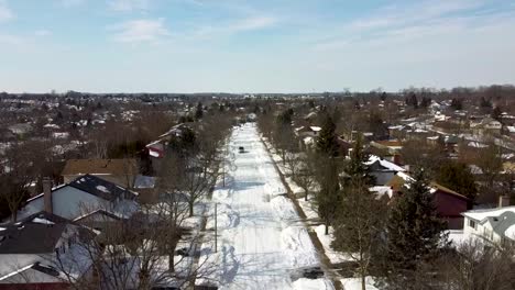 Aerial-view-of-a-van-driving-down-a-snow-packed-road-in-a-subdivision