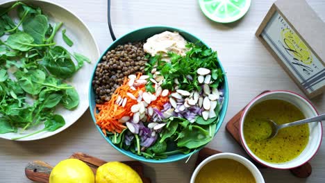 creating a salad adding lentils hummus to plate with spinach and carrots slices cilantro onions sliced almonds dressing lemons