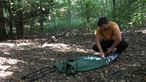 close-up slow motion of a tourist rolling up a tent at forest campsite and packing up to leave