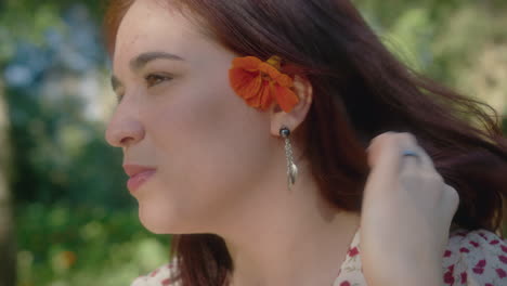 woman puts an orange flower behind her left ear and smiles