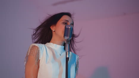 a female singer in a white gown passionately sings with her hands raised and hair flicked back, expressing deep emotions. against a grey background