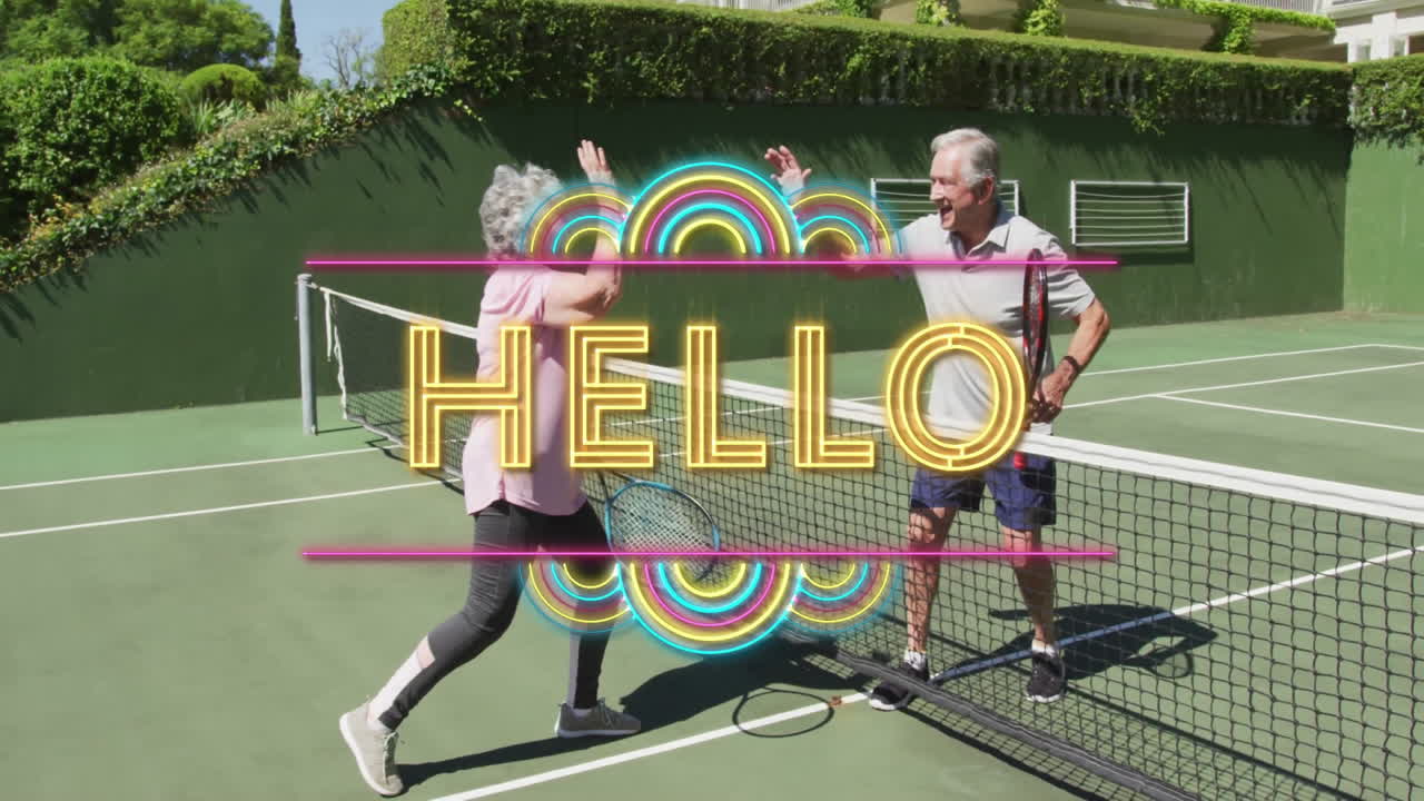 Senior couple raising rackets and high-fiving over net, promoting health with neon HELLO graphic