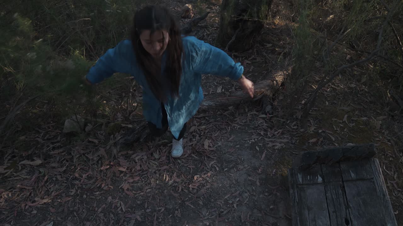 Aerial close-up of a girl trekking through Warrandyte's dense forest vegetation. The dynamic drone shot captures her cautious steps amid natural foliage, showcasing a serene outdoor adventure