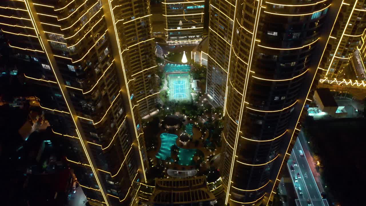 Aerial footage of Rockwell Center skyscrapers in Makati, Metro Manila, glowing with lights at night, pool and surrounded by the vibrant energy of the city skyline.