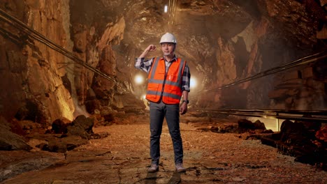 full body of asian male engineer with safety helmet flexing his bicep and smiling to camera while standing in underground mine tunnel