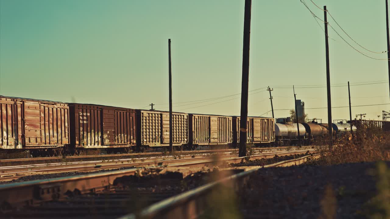 Antiguo tren de carga con vagones cisterna de petróleo deteniéndose en un patio ferroviario industrial abandonado y vacío.